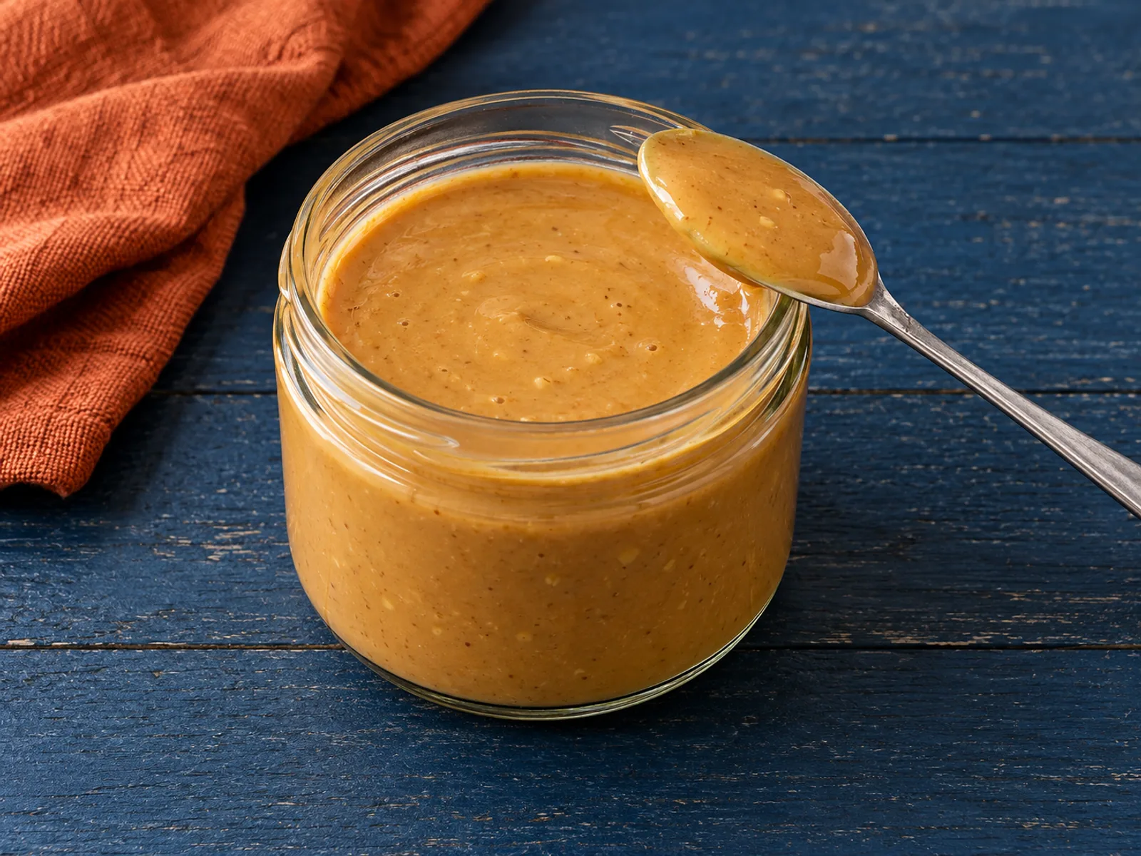 Smooth tan ginger peanut sauce with tiny ginger flecks in an open glass jar, without toppings